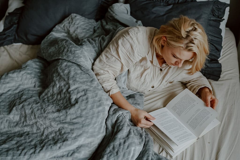 Kobieta czytająca w łóżku książkę, leżąca pod kołdrą obciążeniową