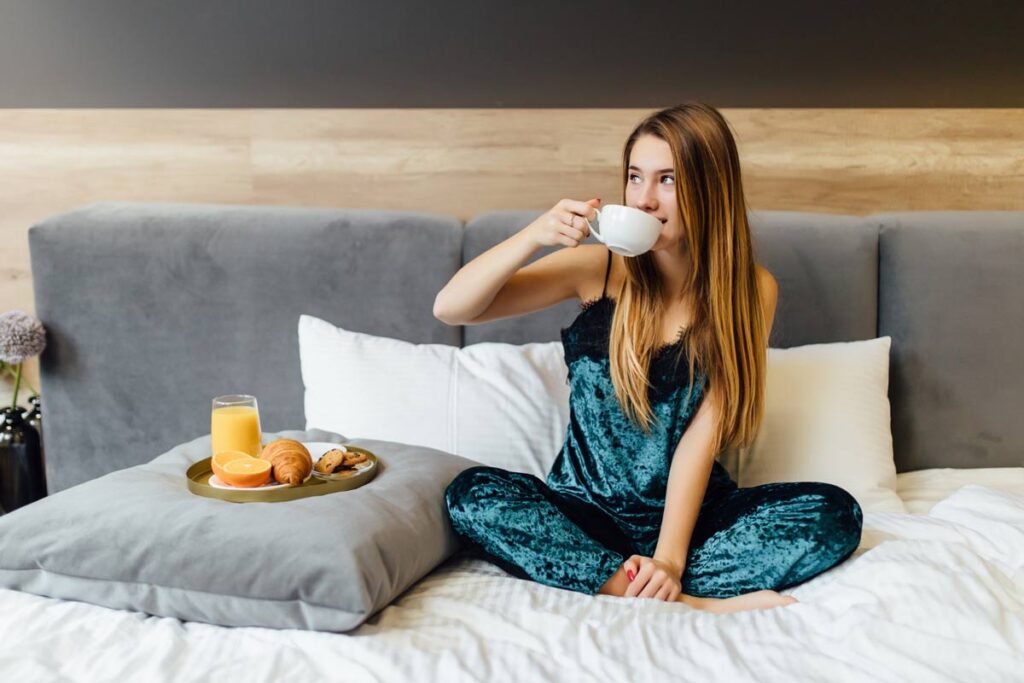 Kobieta siedząca na łóżku, pijąca kawę i zastanawiająca się co jeść, żeby dobrze spać