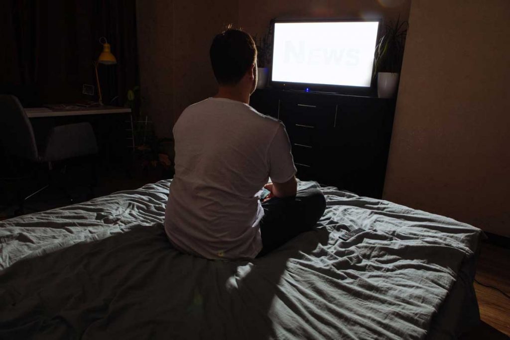 mężczyzna siedzi w nocy na łóżku i wpatruje się we włączony ekran telewizora